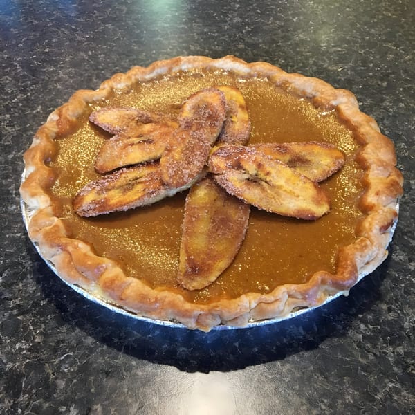 A pumpkin pie with a golden-brown crust and sugared banana slices arranged in a bow shape.