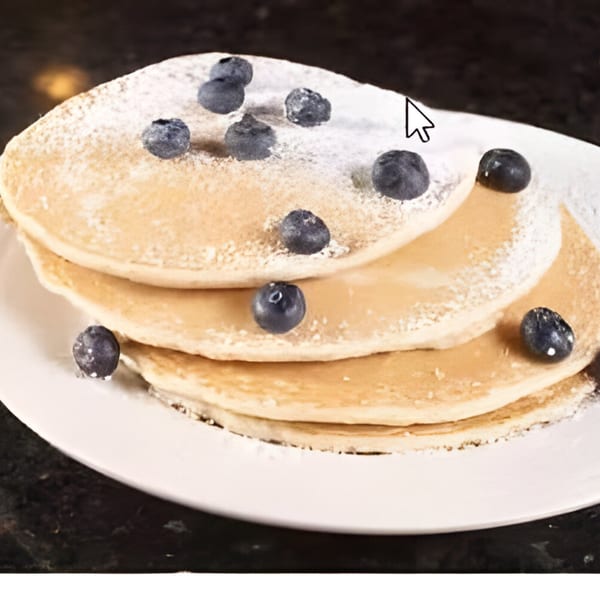 Stack of three pancakes topped with powdered sugar and fresh blueberries on a white plate.