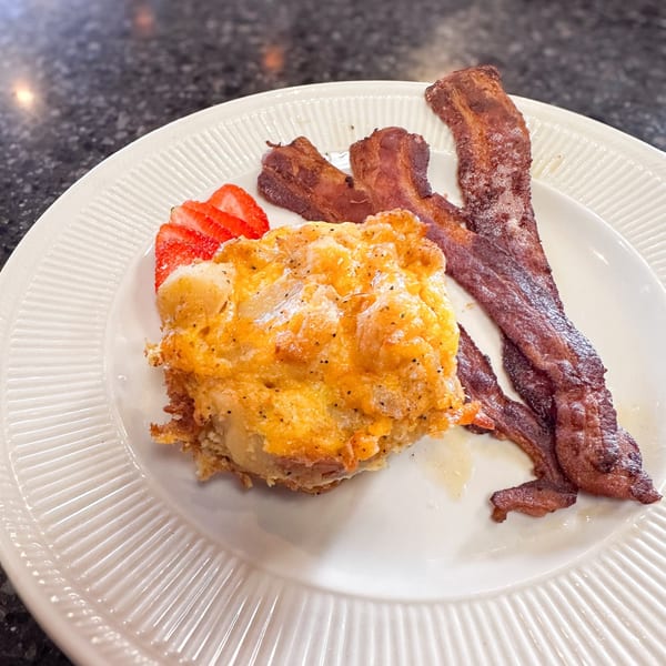 A breakfast plate with cheesy hash browns, crispy bacon, and sliced strawberries.