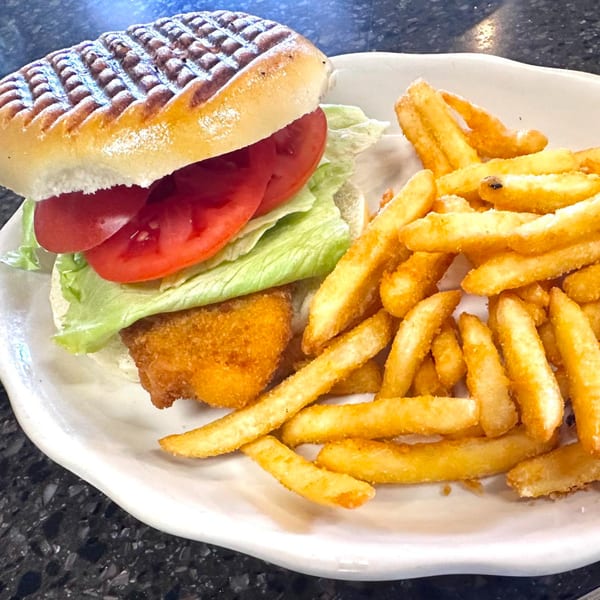A grilled chicken sandwich with lettuce and tomato, served with a side of golden french fries.